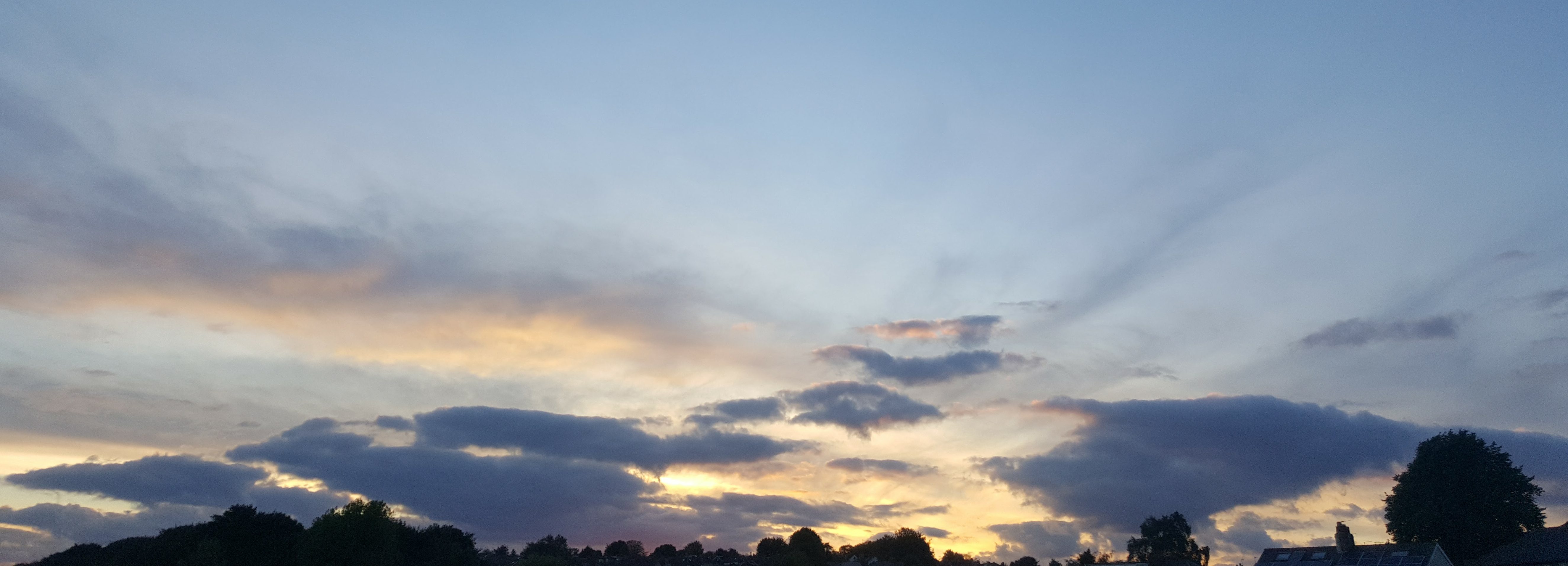 Sunset sky with scattered clouds above darkened treetops and rooftops