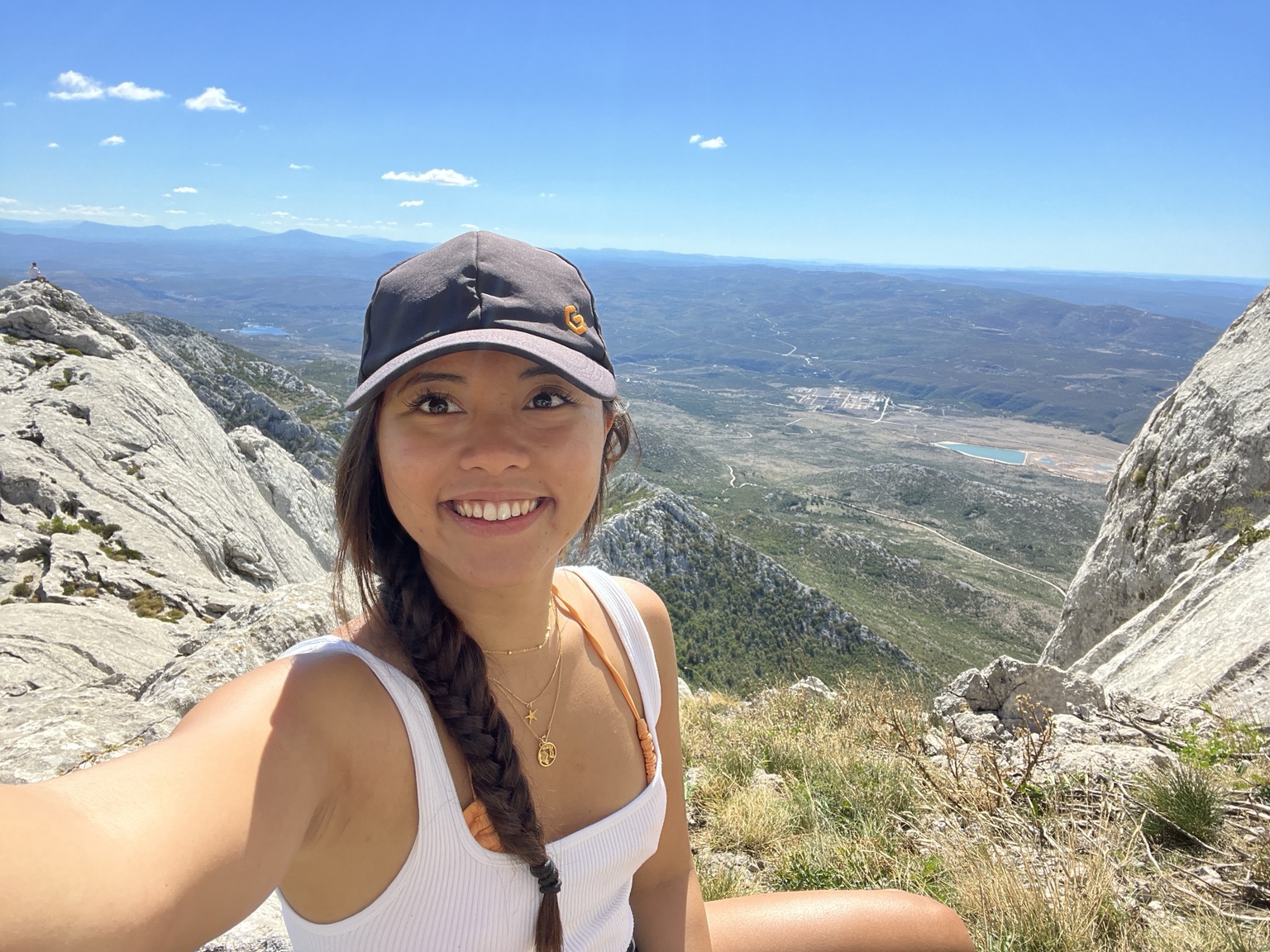 Pauline smiling at the top of a rocky mountain during a hike in Croatia, with the landscape and sea visible behind her