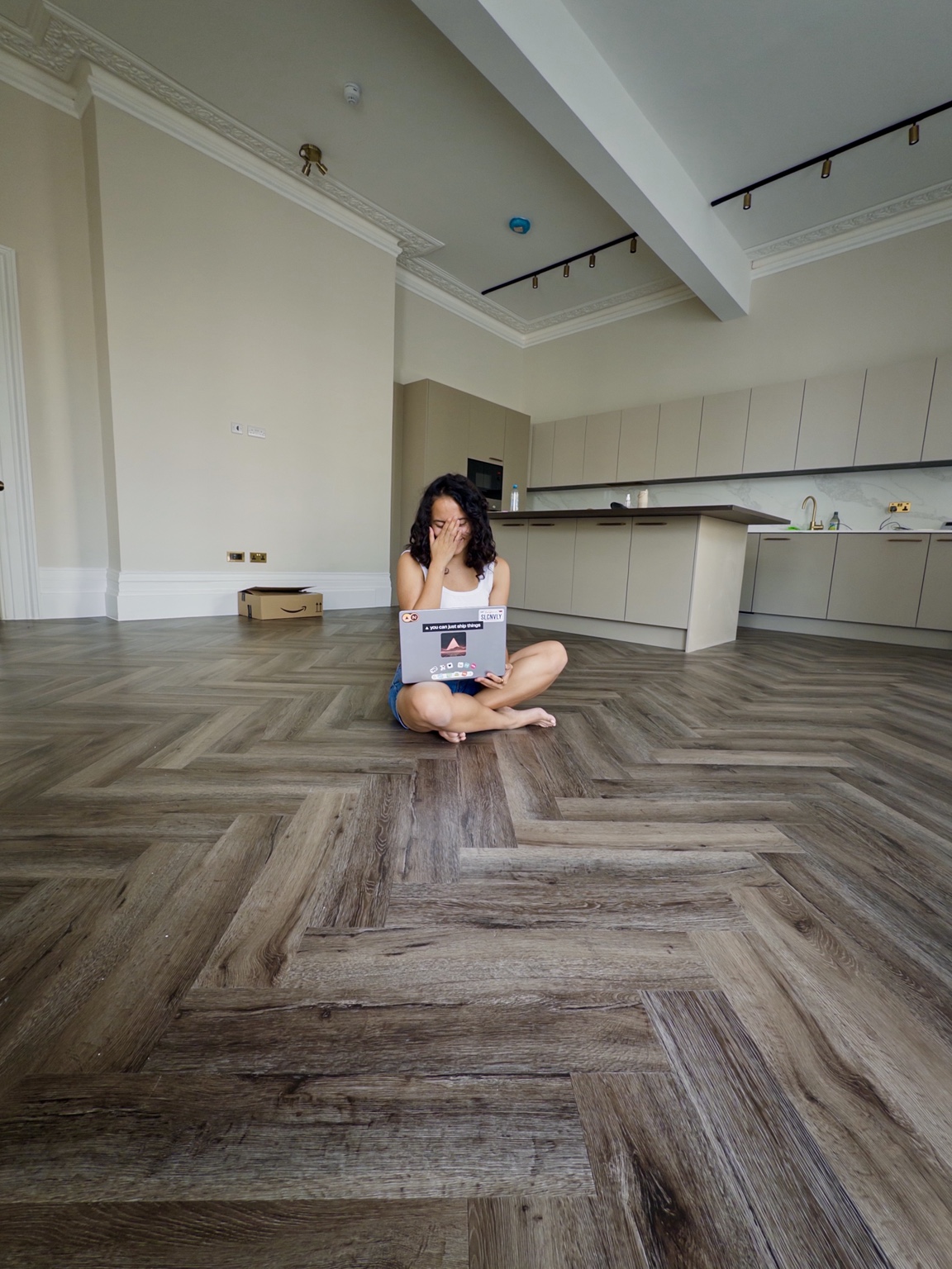Pauline sitting with her laptop on the floor of her largely empty new apartment by the sea